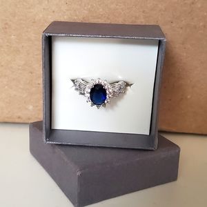 Oval Blue Saphire w/ Swarovski Crystal halo flanked w/ more Swarovski Crystals.